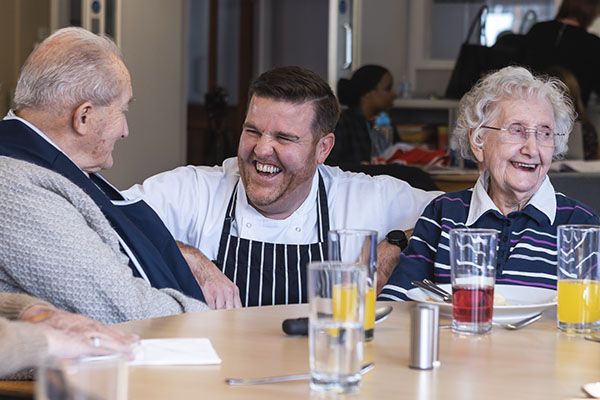 A chef sitting between 2 care home residents and laughing