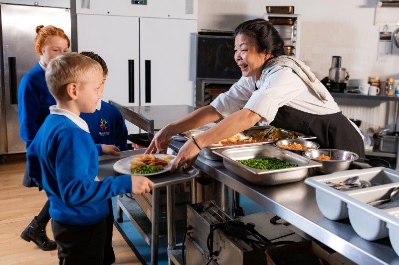 School chef serving food to children in uniform