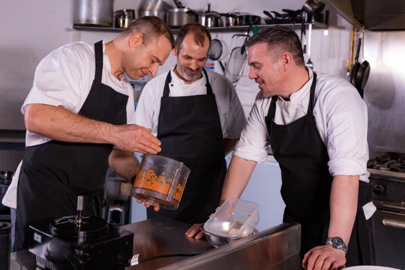 three chefs cooking together in a restaurant kitchen